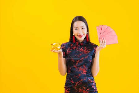 Foto de Retrato hermosa joven mujer asiática usar vestido chino mostrar oro alcancía y rojo letra en amarillo aislado fondo - Imagen libre de derechos