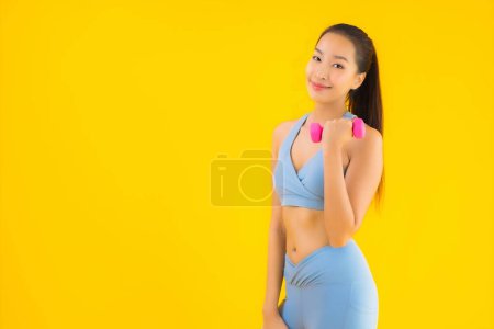 Photo for Portrait beautiful young asian woman with dumbbell and sportwear ready for exercise on yellow isolated background - Royalty Free Image