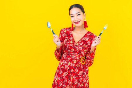 Foto de Retrato hermosa joven asiática mujer con cuchara y tenedor sobre fondo amarillo - Imagen libre de derechos