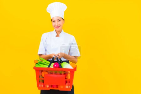 Téléchargez les photos : Portrait belle jeune femme chef asiatique avec panier d'épicerie du supermarché sur fond jaune isolé - en image libre de droit