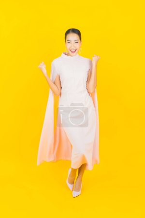 Téléchargez les photos : Portrait belle jeune femme asiatique sourire avec beaucoup d'action sur fond jaune - en image libre de droit