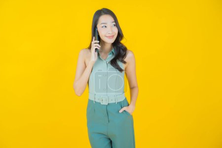 Téléchargez les photos : Portrait belle jeune femme asiatique sourire avec téléphone portable intelligent sur fond de couleur - en image libre de droit