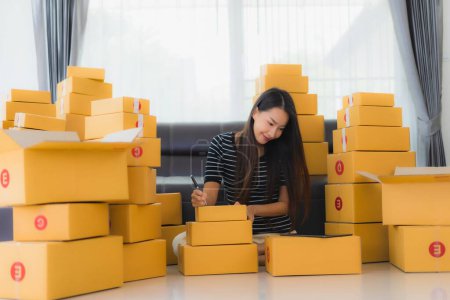 Foto de Retrato hermosa mujer asiática joven con envase de cartón paquete caja de embalaje prepararse para el envío para el cliente en línea de compras en la sala de estar - Imagen libre de derechos