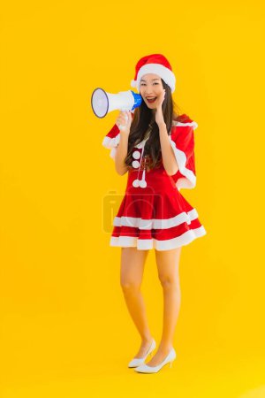 Téléchargez les photos : Portrait belle jeune femme asiatique porter des vêtements de Noël et chapeau utilisation mégaphone sur fond isolé jaune - en image libre de droit