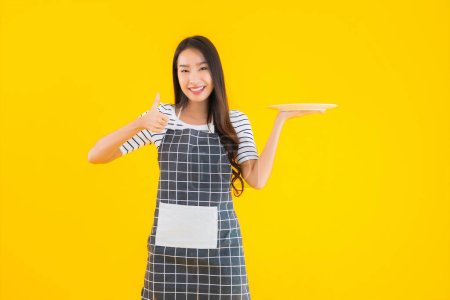 Foto de Retrato hermosa mujer asiática joven con plato blanco o placa sobre fondo aislado amarillo - Imagen libre de derechos