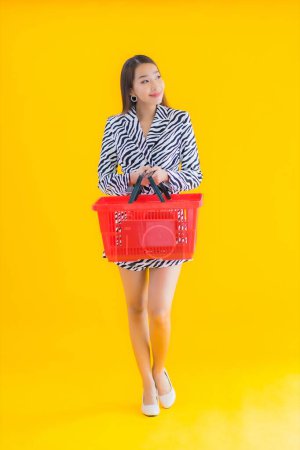 Foto de Retrato hermosa joven asiática mujer con cesta de comestibles para ir de compras en amarillo aislado fondo - Imagen libre de derechos