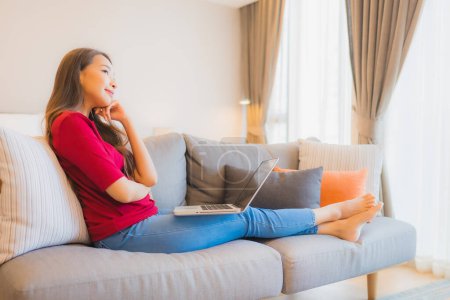 Photo for Portrait beautiful young asian woman use laptop computer on sofa in living area at bedroom interior - Royalty Free Image