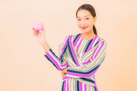 Téléchargez les photos : Portrait belle jeune femme asiatique avec tirelire rose sur fond isolé couleur - en image libre de droit