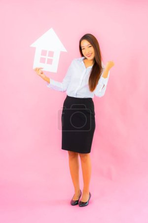 Foto de Retrato hermosa joven asiática mujer espectáculo casa o casa signo en rosa color de fondo - Imagen libre de derechos