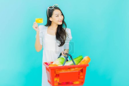 Téléchargez les photos : Portrait belle jeune femme asiatique sourire avec panier d'épicerie du supermarché sur fond de couleur - en image libre de droit