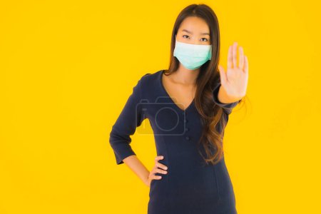 Téléchargez les photos : Portrait belle jeune femme asiatique avec masque pour protéger du coronavirus et covid19 sur fond jaune isolé - en image libre de droit