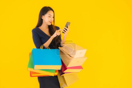 Téléchargez les photos : Portrait belle jeune femme asiatique avec sac à provisions carte de crédit et téléphone portable intelligent fond isolé jaune - en image libre de droit