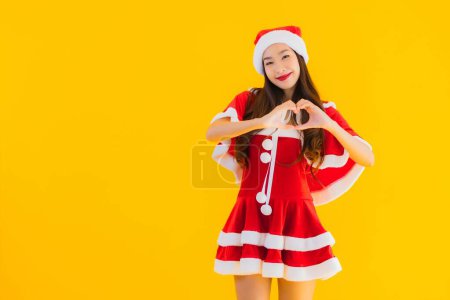 Foto de Retrato hermoso joven asiático navidad ropa y sombrero sonrisa feliz con forma de corazón en amarillo aislado fondo - Imagen libre de derechos