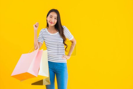 Téléchargez les photos : Portrait belle jeune femme asiatique avec sac à provisions coloré sur fond jaune isolé - en image libre de droit