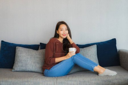 Téléchargez les photos : Portrait belle jeune femme asiatique relax sourire sur canapé dans le salon intérieur - en image libre de droit