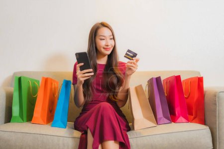 Foto de Retrato hermosa joven mujer asiática sonrisa con tarjeta de crédito, teléfono y bolsas de compras - Imagen libre de derechos