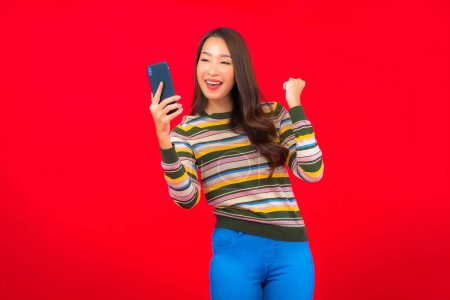 Téléchargez les photos : Portrait belle jeune femme asiatique avec téléphone mobile intelligent sur fond rouge - en image libre de droit