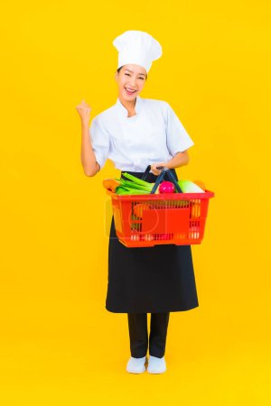 Photo for Portrait beautiful young asian chef woman with grocery basket from supermarket on yellow isolated background - Royalty Free Image