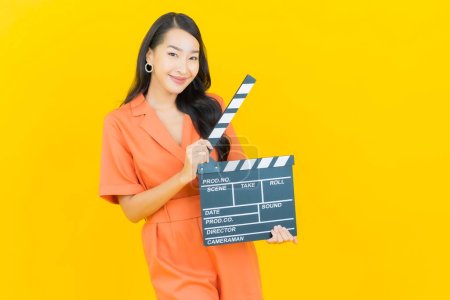 Téléchargez les photos : Portrait belle jeune femme asiatique sourire avec film ardoise plaque de coupe sur fond jaune - en image libre de droit