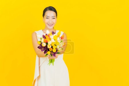 Téléchargez les photos : Portrait belle jeune femme asiatique sourire avec fleur sur fond de couleur jaune - en image libre de droit