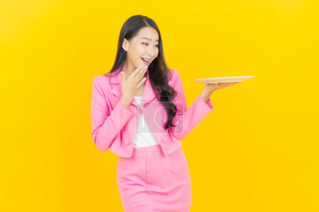 Photo for Portrait beautiful young asian woman smile with empty plate dish on yellow color background - Royalty Free Image