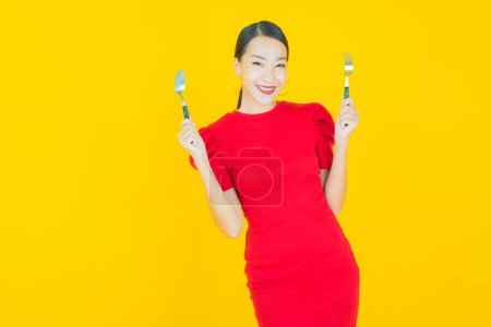 Téléchargez les photos : Portrait belle jeune femme asiatique sourire avec cuillère et fourchette sur fond de couleur - en image libre de droit