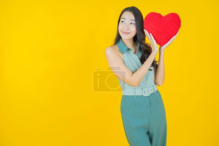 Foto de Retrato hermosa joven asiática mujer sonrisa con corazón almohada forma en color fondo - Imagen libre de derechos