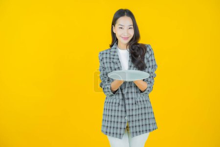 Téléchargez les photos : Portrait belle jeune femme asiatique sourire avec plat vide sur fond de couleur - en image libre de droit