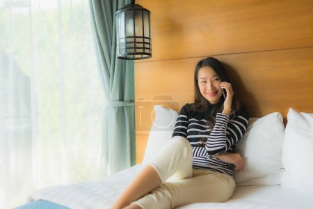 Foto de Retrato joven mujer asiática utilizando el teléfono móvil inteligente en la cama en el interior del dormitorio - Imagen libre de derechos