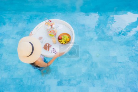 Téléchargez les photos : Portrait belle jeune femme asiatique profiter avec thé après-midi ou petit déjeuner flottant sur la piscine dans la station hôtelière - en image libre de droit