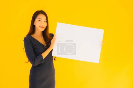 Téléchargez les photos : Portrait belle jeune femme asiatique avec bannière de carte de panneau d'affichage vide et vide sur fond isolé jaune - en image libre de droit