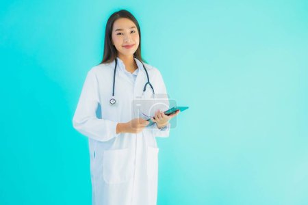 Téléchargez les photos : Portrait belle jeune femme asiatique médecin avec stéthoscope et tablette intelligente pour une utilisation à l'hôpital et la clinique sur fond bleu isolé - en image libre de droit