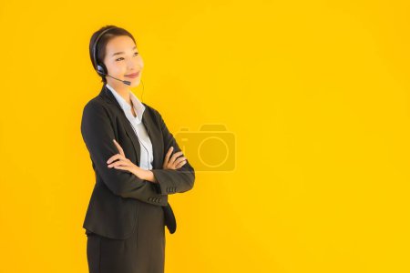 Foto de Retrato hermosa joven mujer asiática de negocios con auriculares o auriculares para call center o telemarketing sobre fondo aislado amarillo - Imagen libre de derechos