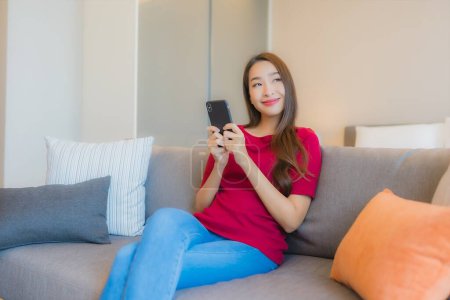 Photo for Portrait beautiful young asian woman use smart mobile phone on sofa in living area at bedroom interior - Royalty Free Image