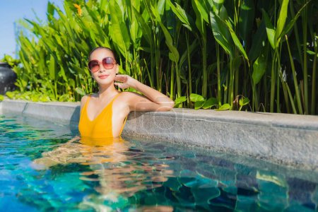 Téléchargez les photos : Portrait belle jeune femme asiatique se détendre sourire heureux autour de la piscine extérieure dans la station hôtelière pour les vacances de loisirs - en image libre de droit