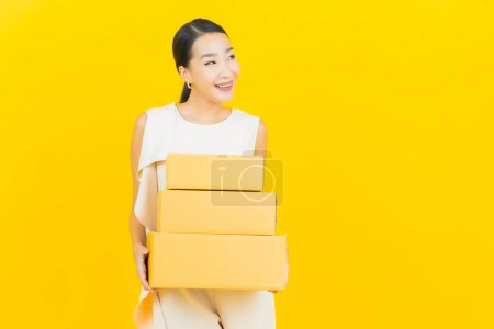 Téléchargez les photos : Portrait belle jeune femme asiatique avec boîte prête pour l'expédition sur fond jaune - en image libre de droit