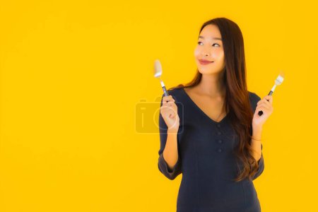 Téléchargez les photos : Portrait belle jeune femme asiatique avec cuillère et fourchette prête à manger sur fond jaune isolé - en image libre de droit