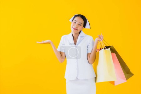 Photo for Portrait beautiful young asian woman thai nurse with shopping bag and credit card on yellow isolated background - Royalty Free Image
