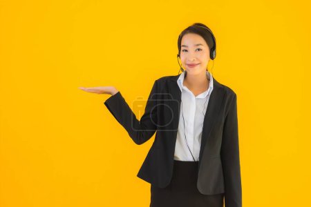 Foto de Retrato hermosa joven mujer asiática de negocios con auriculares o auriculares para call center o telemarketing sobre fondo aislado amarillo - Imagen libre de derechos