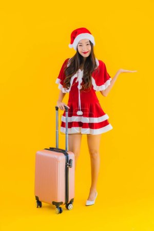 Téléchargez les photos : Portrait belle jeune femme asiatique porter des vêtements de Noël chapeau avec sac à bagages et téléphone intelligent prêt pour Voyage sur fond isolé jaune - en image libre de droit