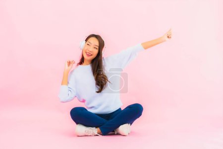 Téléchargez les photos : Portrait belle jeune femme asiatique utiliser téléphone portable intelligent avec casque pour écouter de la musique sur fond rose - en image libre de droit