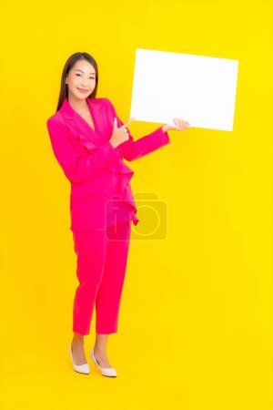 Foto de Retrato hermosa joven asiática mujer con vacío blanco cartel en amarillo aislado fondo - Imagen libre de derechos