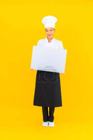 Téléchargez les photos : Portrait belle jeune asiatique chef femme avec blanc vide panneau d'affichage sur fond jaune isolé - en image libre de droit