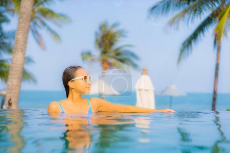 Téléchargez les photos : Portrait belle jeune femme asiatique relax sourire profiter des loisirs autour de la piscine presque mer plage océan vue pour les vacances de loisirs - en image libre de droit