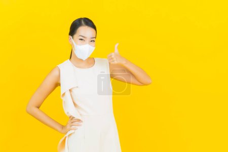 Téléchargez les photos : Portrait belle jeune femme asiatique avec masque pour protéger covid19 ou virus sur fond de couleur jaune - en image libre de droit