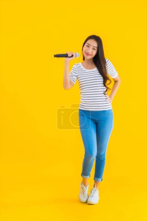 Téléchargez les photos : Portrait belle jeune femme asiatique chantant avec microphone et casque sur fond jaune isolé - en image libre de droit
