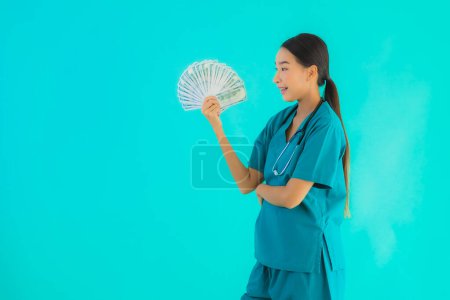 Foto de Retrato hermosa joven asiática médico mujer mostrar dinero y dinero en efectivo en azul aislado fondo - Imagen libre de derechos