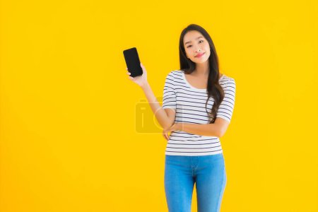 Foto de Retrato hermosa joven asiática mujer sonrisa feliz uso inteligente móvil en amarillo aislado fondo - Imagen libre de derechos