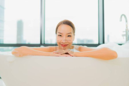 Téléchargez les photos : Portrait belle jeune femme asiatique relax sourire loisirs dans la baignoire dans salle de bain intérieur - en image libre de droit
