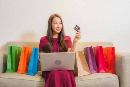 Foto de Retrato hermosa joven mujer asiática sonrisa con tarjeta de crédito, ordenador portátil y bolsas de compras - Imagen libre de derechos